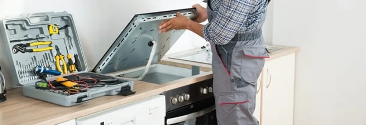 Cooktop repair technician lifting a built-in stovetop for service in Fresno, CA