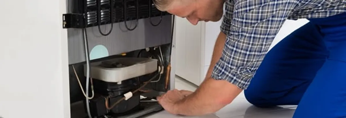 Refrigerator repair technician servicing the compressor and condenser area in Fresno, CA