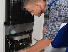 Refrigerator repair technician servicing the compressor and condenser area in Fresno, CA