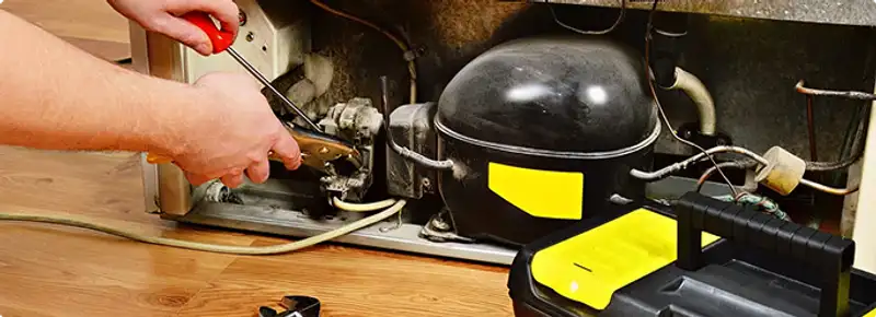 Refrigerator repair technician fixing the compressor and wiring in Fresno, CA